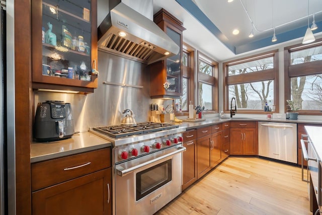 kitchen featuring wall chimney exhaust hood, sink, decorative light fixtures, light hardwood / wood-style flooring, and stainless steel appliances