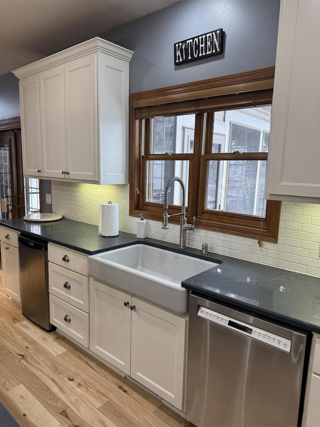 kitchen with dark countertops, white cabinets, dishwasher, and a sink