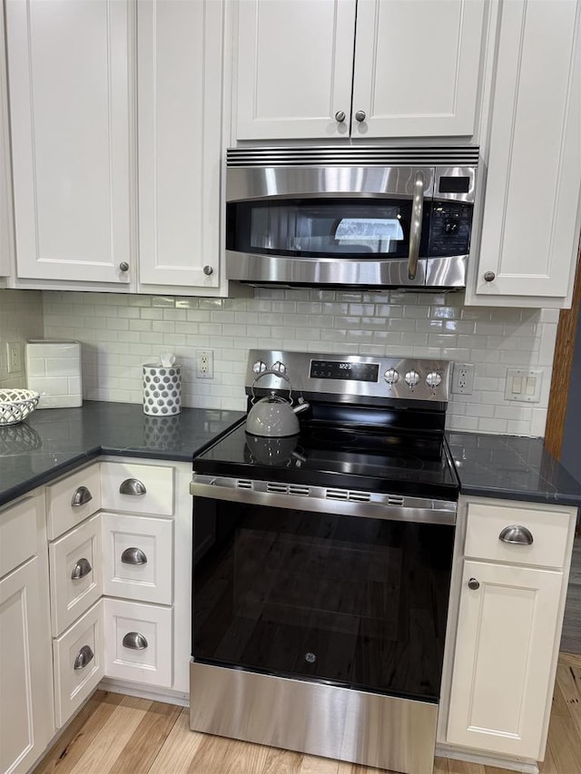 kitchen with stainless steel appliances, light wood-style floors, decorative backsplash, and white cabinets