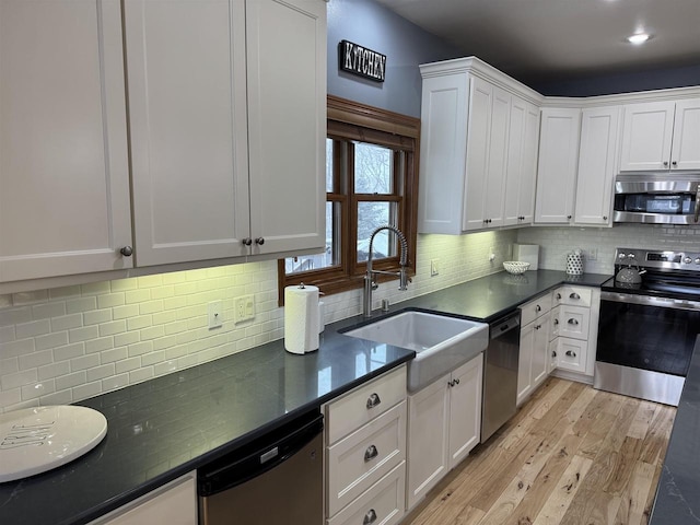 kitchen featuring dark countertops, appliances with stainless steel finishes, white cabinets, and a sink