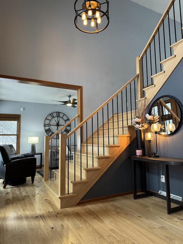 stairs with ceiling fan with notable chandelier, wood finished floors, and a towering ceiling