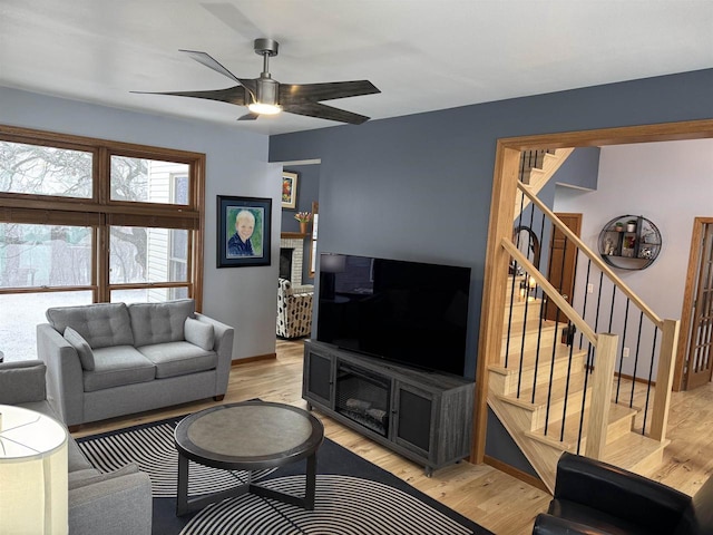 living area with light wood finished floors, ceiling fan, and stairway