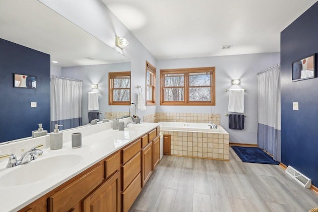 full bath with wood finished floors, a sink, visible vents, a bath, and double vanity