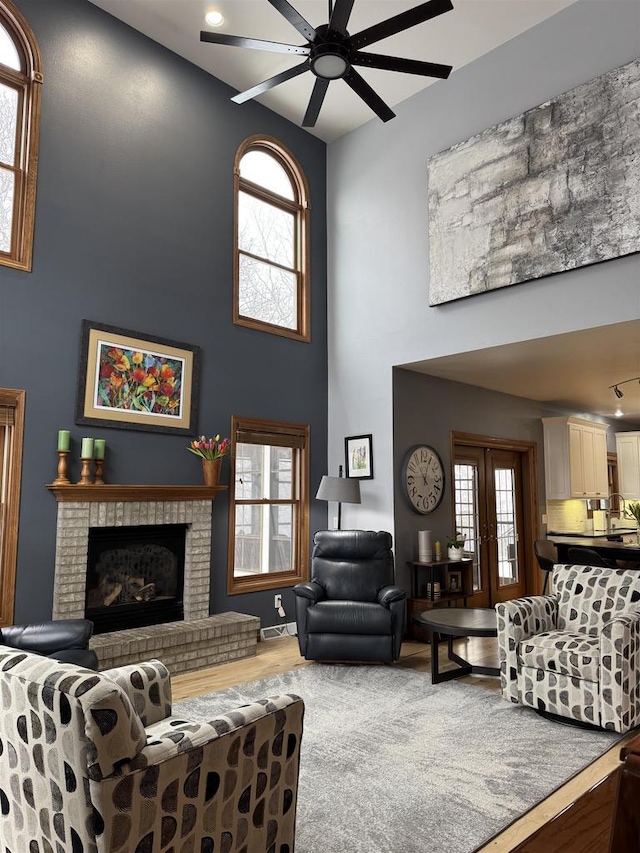 living room featuring a fireplace, visible vents, a towering ceiling, ceiling fan, and wood finished floors