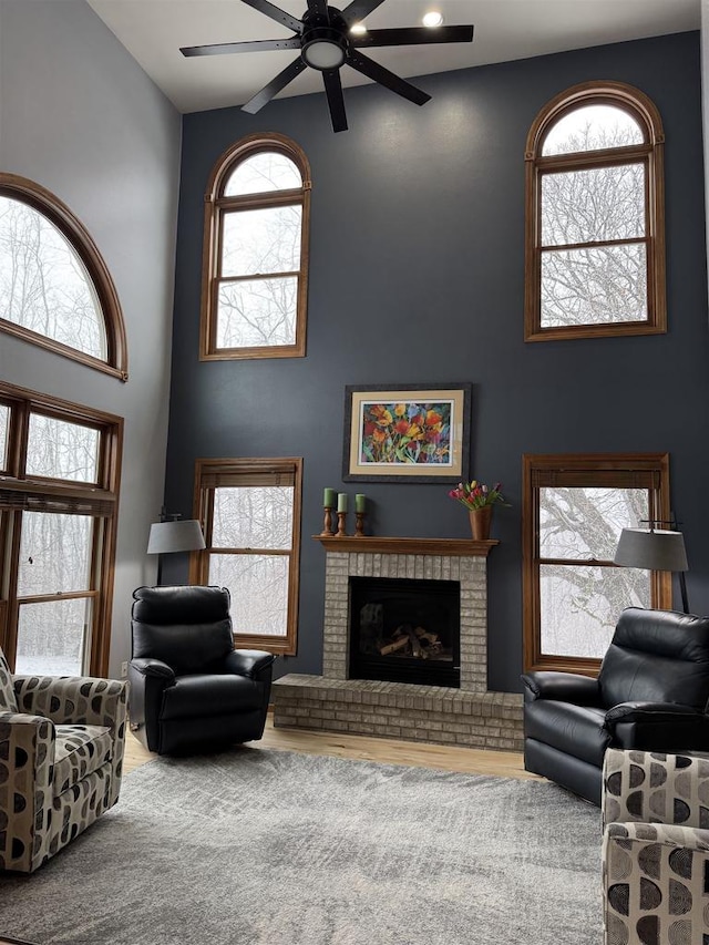 living room with ceiling fan, a high ceiling, and a brick fireplace