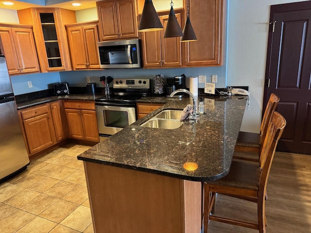 kitchen with pendant lighting, sink, appliances with stainless steel finishes, a kitchen breakfast bar, and dark stone counters