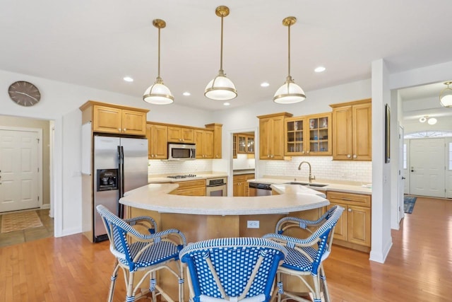 kitchen with appliances with stainless steel finishes, a kitchen bar, sink, and light wood-type flooring