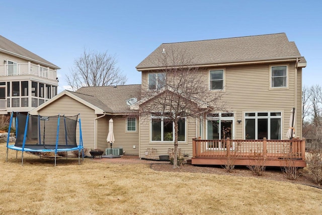 rear view of property featuring a sunroom, a deck, a trampoline, and a lawn