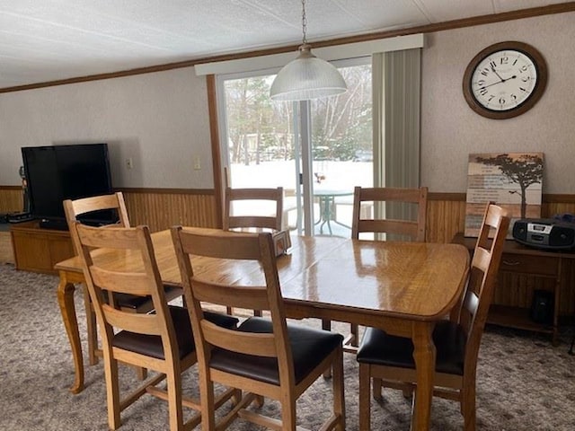 carpeted dining room featuring ornamental molding and wood walls