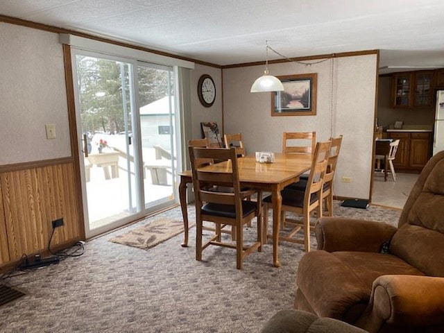 dining space featuring ornamental molding, light colored carpet, and wood walls