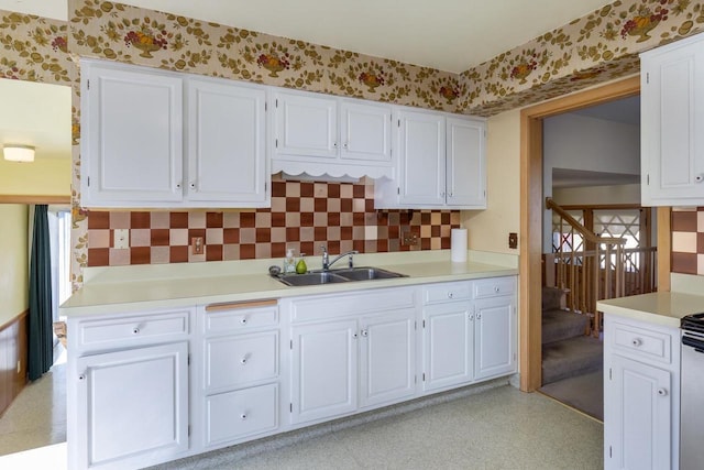 kitchen with wallpapered walls, white cabinets, a sink, and light countertops