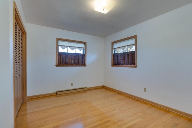 unfurnished bedroom with light wood-type flooring, baseboards, baseboard heating, and a closet