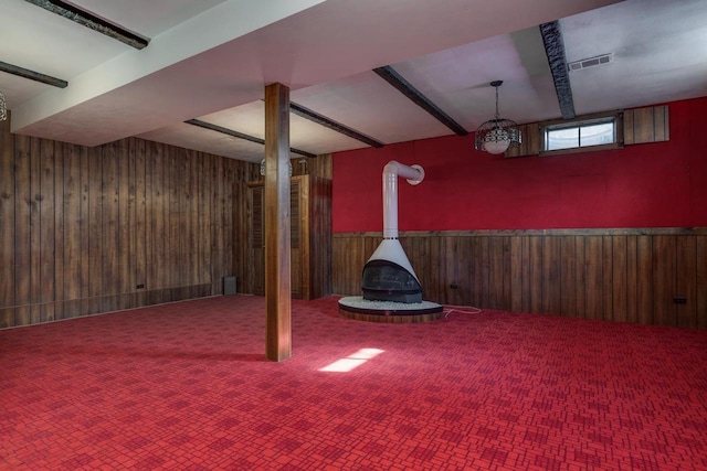 below grade area with a wood stove, a wainscoted wall, carpet, and wooden walls