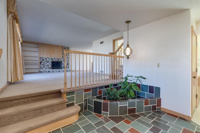 stairway featuring carpet flooring, a stone fireplace, and baseboards