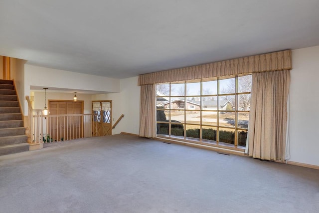 unfurnished living room featuring stairway, carpet, and visible vents