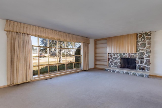 unfurnished living room with carpet floors, visible vents, a stone fireplace, and baseboards