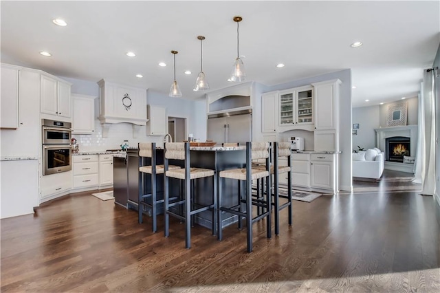 kitchen featuring appliances with stainless steel finishes, white cabinets, hanging light fixtures, a kitchen island with sink, and light stone countertops