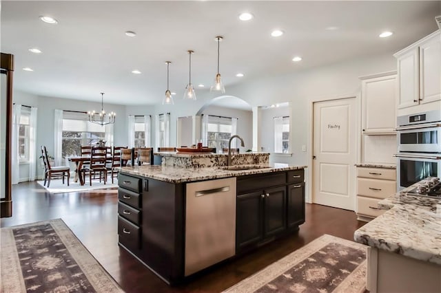 kitchen with sink, light stone counters, appliances with stainless steel finishes, pendant lighting, and a kitchen island with sink