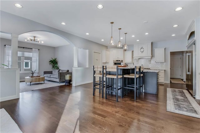 kitchen with a kitchen breakfast bar, an island with sink, pendant lighting, oven, and white cabinets