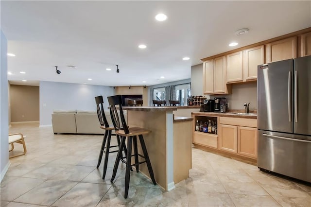 kitchen with sink, stainless steel refrigerator, a kitchen breakfast bar, light tile patterned flooring, and light brown cabinets