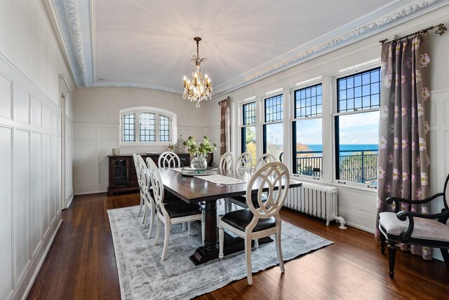 dining area with radiator, crown molding, dark wood-type flooring, a water view, and a notable chandelier