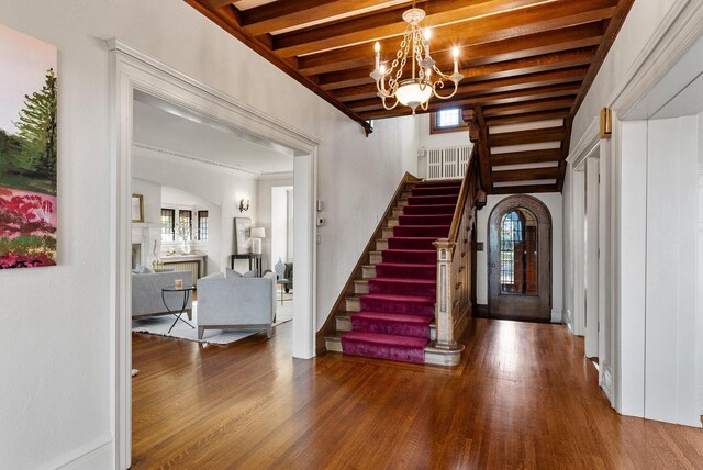 foyer entrance with hardwood / wood-style flooring, a chandelier, and beamed ceiling