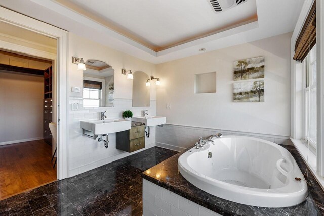 bathroom featuring tiled tub, double sink, and a tray ceiling