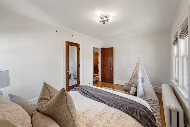 bedroom with crown molding, radiator heating unit, and hardwood / wood-style floors