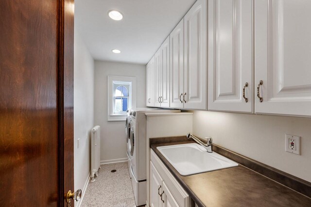 washroom with sink, radiator heating unit, washing machine and dryer, and cabinets