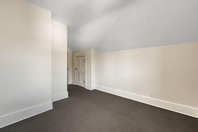 bonus room with vaulted ceiling and dark colored carpet