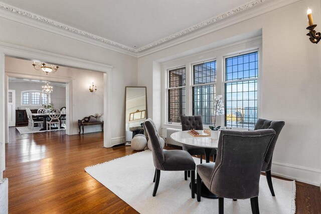 dining room with ornamental molding, wood-type flooring, radiator heating unit, and a notable chandelier