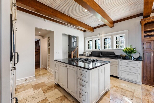 kitchen with sink, beam ceiling, stainless steel gas cooktop, white cabinets, and a kitchen island