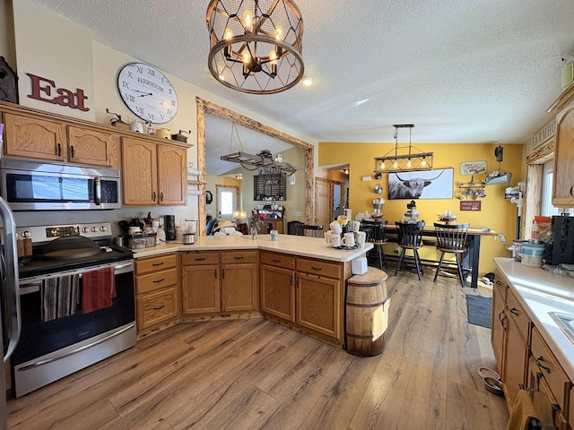 kitchen with appliances with stainless steel finishes, vaulted ceiling, a wealth of natural light, light wood-type flooring, and pendant lighting