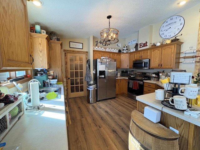 kitchen featuring a notable chandelier, a textured ceiling, decorative light fixtures, stainless steel appliances, and dark wood-type flooring