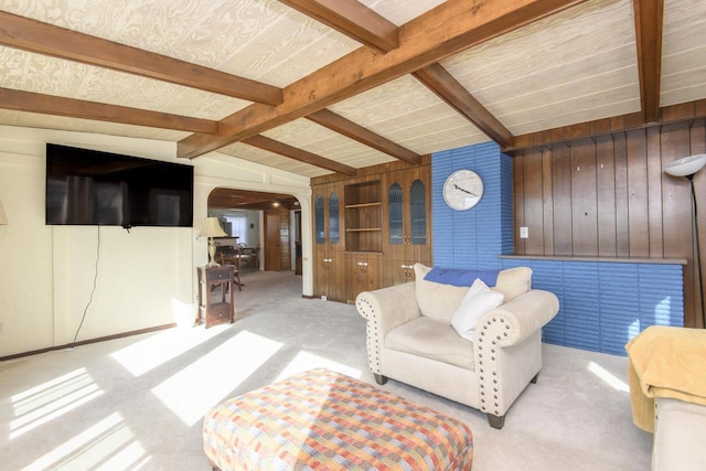 living room with arched walkways, lofted ceiling with beams, light carpet, and wooden walls