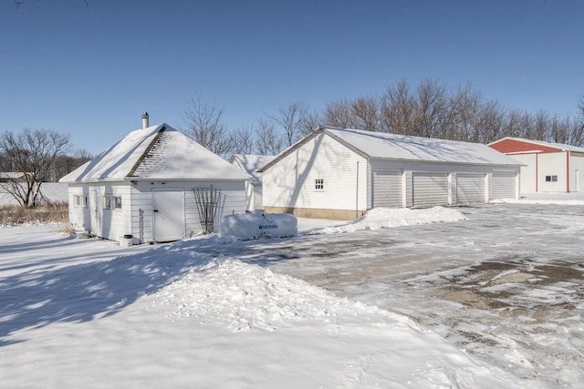 view of snow covered exterior featuring a detached garage and an outdoor structure