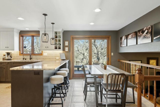 kitchen featuring sink, hanging light fixtures, backsplash, light stone countertops, and white cabinets