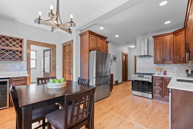 kitchen featuring sink, appliances with stainless steel finishes, decorative backsplash, wall chimney exhaust hood, and light wood-type flooring