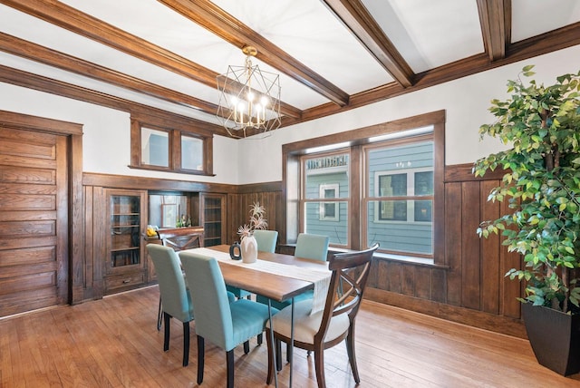 dining space featuring light hardwood / wood-style flooring, an inviting chandelier, beam ceiling, ornamental molding, and wood walls