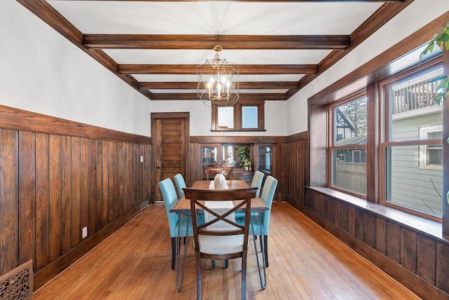 dining room featuring beamed ceiling, wood walls, and light hardwood / wood-style flooring