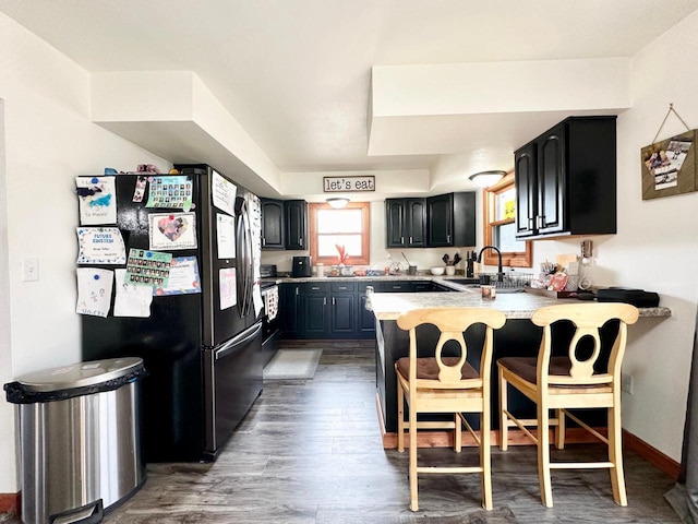 kitchen featuring a breakfast bar, sink, fridge, dark hardwood / wood-style floors, and kitchen peninsula