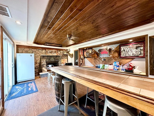 bar with wood-type flooring, tile countertops, wooden ceiling, fridge, and a tray ceiling