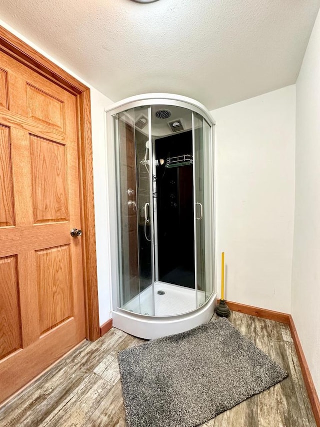 bathroom with hardwood / wood-style flooring, a shower with door, and a textured ceiling