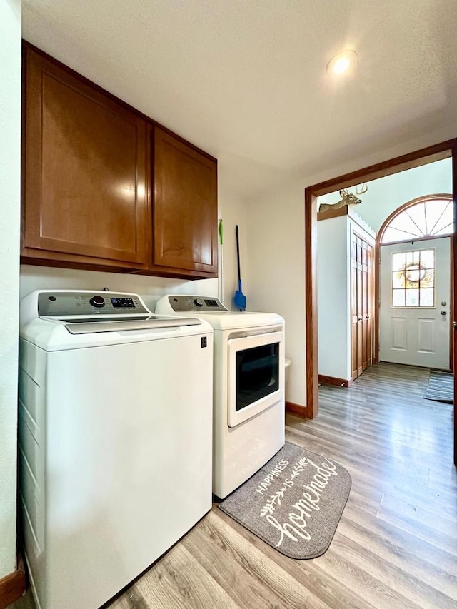 washroom with cabinets, washing machine and dryer, and light hardwood / wood-style floors