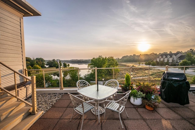 patio terrace at dusk with a water view, a balcony, and grilling area