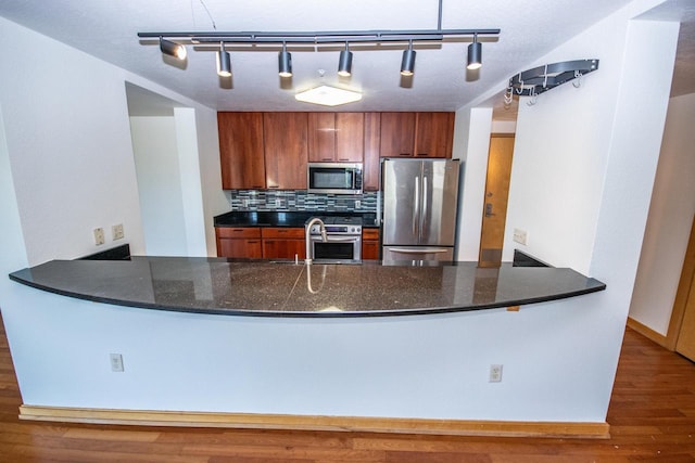 kitchen featuring sink, dark stone counters, stainless steel appliances, hanging light fixtures, and tasteful backsplash