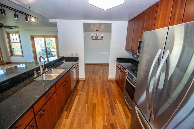 kitchen featuring dark stone countertops, sink, light hardwood / wood-style floors, stainless steel appliances, and hanging light fixtures