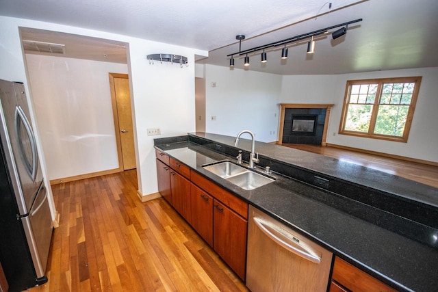 kitchen with dark stone countertops, sink, light hardwood / wood-style floors, stainless steel appliances, and a fireplace