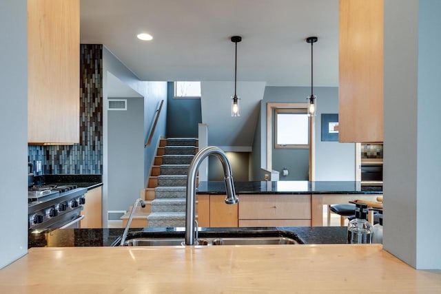 kitchen featuring plenty of natural light, stainless steel gas range oven, tasteful backsplash, light brown cabinetry, and a sink