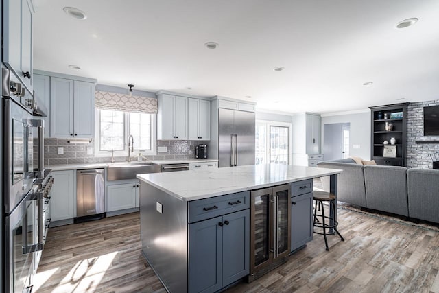 kitchen featuring stainless steel appliances, a kitchen island, sink, light stone counters, and beverage cooler